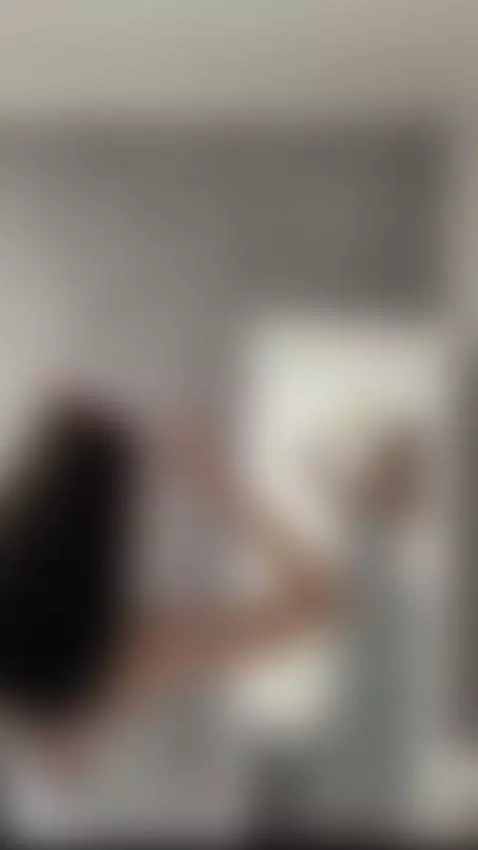 Arms raised high as she ties her hair back by sofits